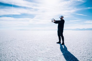 Bonneville Tuz Düzlükleri 'nde vakit geçirirken VR gözlüklerini test etmek için tablet kullanan siyah elbiseli tam boy erkek.