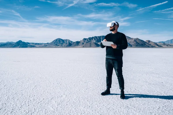 Sanal gerçeklik gözlüklü, modern tabletli, Bonneville Tuz Düzlükleri 'nde modern aletler kullanan sakallı bir erkek.