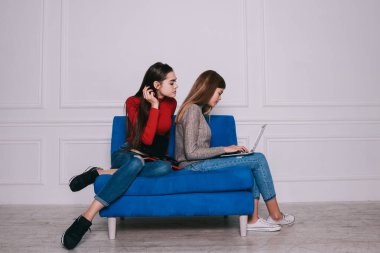 Tüm vücut konsantre olmuş, uzun saçlı, günlük kıyafetlerle ev ödevlerini laptopla ve defterlerle hazırlarken beyaz odadaki mavi koçun üzerinde oturuyordu.