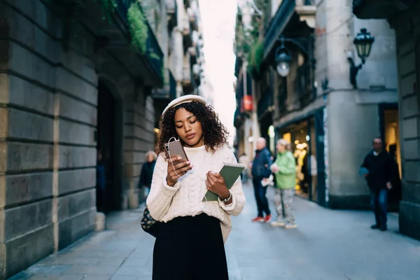 街の通りに立って流行の服で魅力的な暗い肌の女性スマートフォンでメッセージやニュースを読んで 美しいアフリカ系アメリカ人の100万人の女性は 呼び出しのための携帯電話上の番号をダイヤル — ストック写真