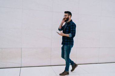 Elektronik kulaklıklı beyaz tenli adam, tanıtım alanında müzik dinlemek için cep telefonu uygulaması kullanıyor, milenyum erkek turisti, akıllı telefonlara bağlanıp müzik listesinin keyfini çıkarıyor.