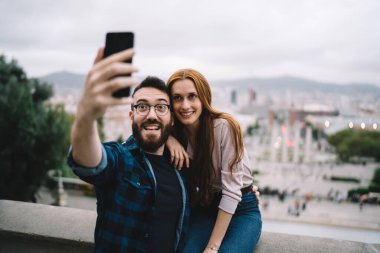 Mutlu etki blogcuları, seyahat yaşam tarzıyla ilgili video blogu çekerken gülümsüyor. Neşeli erkek ve kadın milenyumlar, mobil teknoloji ile selfie içeriği oluşturdukları için seyahat yolculuğunun keyfini çıkarıyorlar.