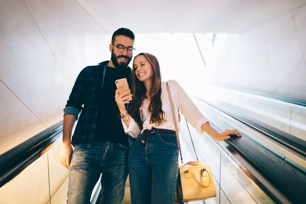 快乐的嬉皮士女孩在大都市自动扶梯上与白人男友共享内容 快乐的男性和女性在社交媒体上浏览 — 图库照片