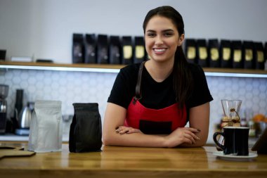 Küçük işletme kafeteryasının müreffeh bayan sahibinin yarım boy portresi paketler halinde kahve satışı yapan bir kadın garson, barda siparişleri yerine getirmeye hazır bir şekilde bekliyor.