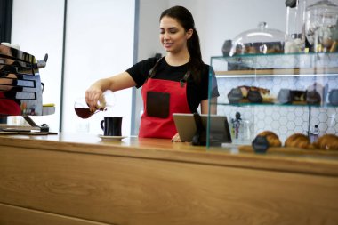 Üniformalı kadın garson, kafeteryadaki barda filtreden fincana kadar profesyonel ekipmanlardan sıcak aroma kahvesi dolduruyor.