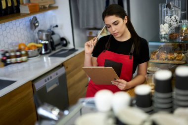 Önlüklü, düşünceli, beyaz kadın garson. Finans raporuna göre kahve dükkanının gelirini analiz ediyor. Düşünceli, güzel bayan barista başvuru formunu kontrol ederken kafası karışmış.