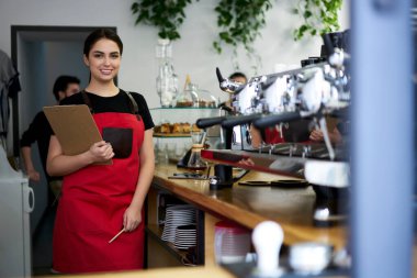 Yarım boy portre, refah içinde beyaz kadın garson, kafeteryada hizmet etmeye hazır, mutlu 20 'li yaşlarda, önlüklü, modern kahve dükkanındaki işinden zevk alan kadın garson.