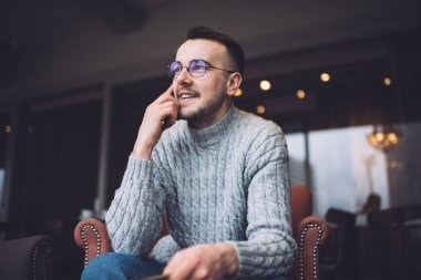 Rahat koltukta oturan ve cep telefonuyla konuşan sıradan giysili ve gözlüklü neşeli sakallı adamın alçak açısı.