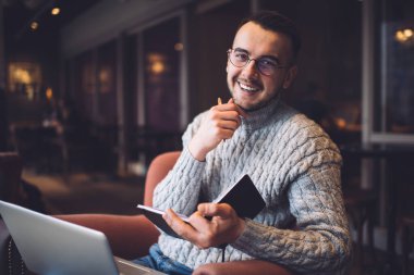 Günlük kıyafet ve göz giysisi içinde mutlu sakallı, uzaktan kumandalı bir işçi. Gülümsüyor ve fotoğraf makinesine bakıyor.