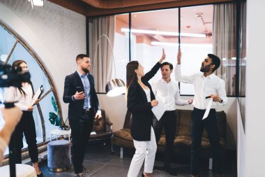 Bir grup başarılı iş arkadaşı resmi olarak giyinirken modern ışık ofisinde başarılı bir anlaşmayı kutlarken beşlik çakıyor.