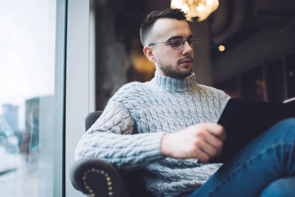 头脑清醒 留着胡子 身穿休闲装和眼镜的男性 坐在舒适的咖啡店里舒适的扶手椅上 专心致志地阅读有趣的书籍 — 图库照片