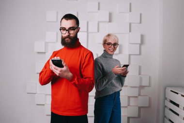 Genç, sakallı bir hippi cep telefonundan arıyor ve neşeli sarışın bir kadın akıllı telefonuna bakıyor ve kameraya bakıyor.