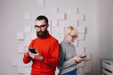 Akıllı gözlüklü genç adam ve kadın üç boyutlu geometrik desenli beyaz duvarın yanında duruyor.