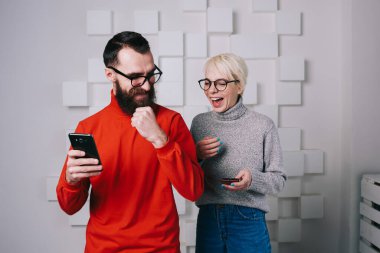 Neşeli genç adam ve kadın şık gündelik kıyafetler ve gözlüklerle gülerken modern ofis odasında işe başlama başarısı ile heyecanlı yumruklar sallıyor.