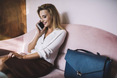 Orta yaşlı kadın işçi rahat koltukta otururken ve cep telefonuyla sohbet ederken şık günlük giysiler içinde aşağıya bakıyor.