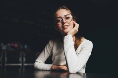 Uzun saçlı, kameraya bakan, karanlıkta oturan ve elini uzatan mutlu bir kadın.