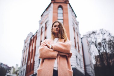 Elleri bağlı, boş vakitleri varken binanın yanında duran kalın montlu, ciddi bir kadının alçak açısı.