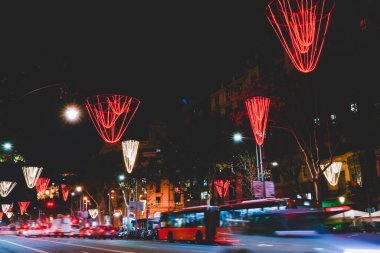 Renkli ışık süslemeleri altında arabalarla ve karanlık bir gecede şehrin sokaklarında parlayan lambalarla dolu pitoresk şehir manzarası.