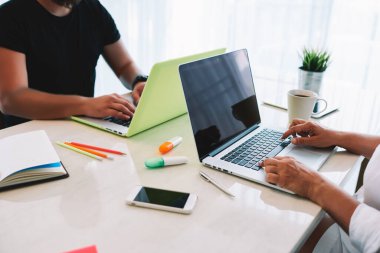 Modern iş yerinde notlar ve kahve eşliğinde dizüstü bilgisayarlar üzerinde çalışırken aynı masada oturan isimsiz etnik iş arkadaşları.