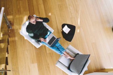 Yukarıdan, hafif apartmandaki koltukta otururken telefonla konuşan ve netbook 'u karıştıran konsantre erkek uzaktan çalışan.