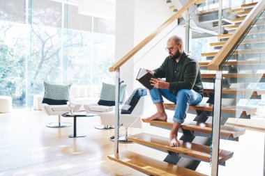 Tüm vücudu sakallı, sıradan kıyafetleri ve gözlükleriyle ilginç bir kitap okuyan ve gün ışığında çatı katında merdiven boşluğunda dinlenen bir adam.