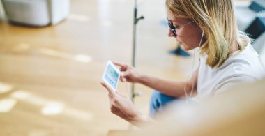 Çevrimiçi video izlerken akıllı telefonu yatay pozisyonda tutan mutlu bayanın arka görüntüsü aydınlık odada boş zaman harcıyor