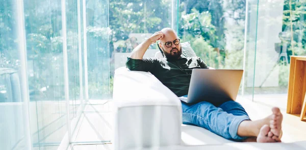 Wide Angle Serious Male Freelancer Touching Head Sitting Sofa Crossed — стоковое фото