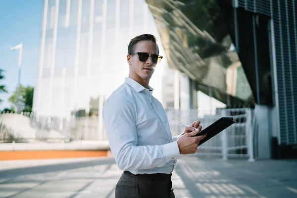 金融区上班时间 穿着时髦太阳镜的英俊男性经理用4G互联网在现代触摸板上对着镜头的半身肖像 时髦的商人带着小玩意 — 图库照片