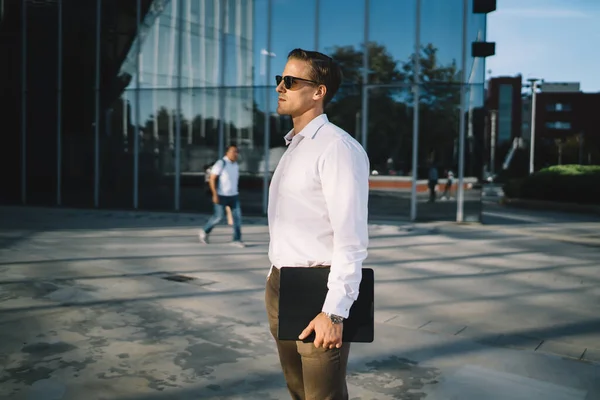 ダウンタウンの都市通りにデジタルタブレットが立っているスマートカジュアル起業家の側面図 金融街で待っている手で現代的なタッチパッドを保持サングラスで白人ビジネスマン — ストック写真