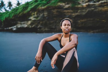 30 'lu yaşlardaki zayıf bir kadın, deniz kıyısının siyah kumlarında dinleniyor. Kaslı vücudu için kardiyo eğitimi almayı düşünüyor. Afrika kökenli Amerikalı kadın koşucu, sabah kıyı şeridinde antrenman yaparken dinleniyor.