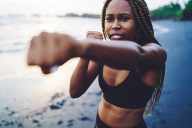 Eşofmanlı Afro-Amerikan formalı kız deniz kıyısında güçlü yumruklar, antrenman sırasında konsantre sporcu kadın eğitimi ve boks, sağlıklı yaşam tarzı kavramı ve amaç için motivasyon.