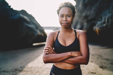 Çekici, Afro-Amerikan fit bir kızın yarım boy portresi. Sıradan figürlü, vücut destekli, pozitif hareketli, koyu tenli, sabah sahili sahillerinde poz veren spor elbiseli bir kadın antrenör.