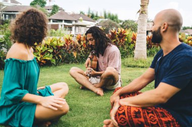 Parktaki yeşil çimlerde oturan, akustik gitarlı ve yazdan keyif alan bir grup çok ırklı insan birbirleriyle konuşurken...