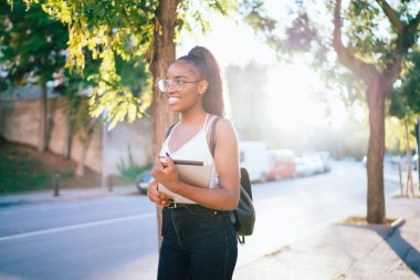 20 'li yaşlardaki mutlu siyah turistlerin arka plandaki manzarası. Şehir caddesinde yürüyorlar ve gülümsüyorlar. Dijital tabletli neşeli yeniyetme kız yeni kasabayı keşfetmek için tek başına seyahatlerin keyfini çıkarıyorlar.