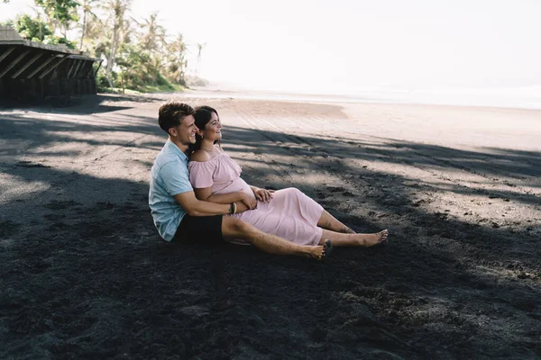 Seitenansicht Ganzkörper Lächelndes Schwangere Paar Trendiger Sommerkleidung Sitzt Schwarzen Sandstrand — Stockfoto