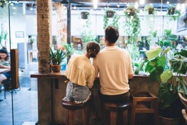 Gündelik kıyafetlerle arka plandaki kadın rahat çalışma alanında ya da kafeteryada birlikte vakit geçirirken yüksek masada oturuyor ve erkek arkadaşlarının omuzlarında dinleniyor.