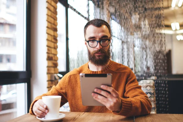 Pensive Male Freelancer Sitting Wooden Table Cup Coffee Browsing Tablet — стоковое фото