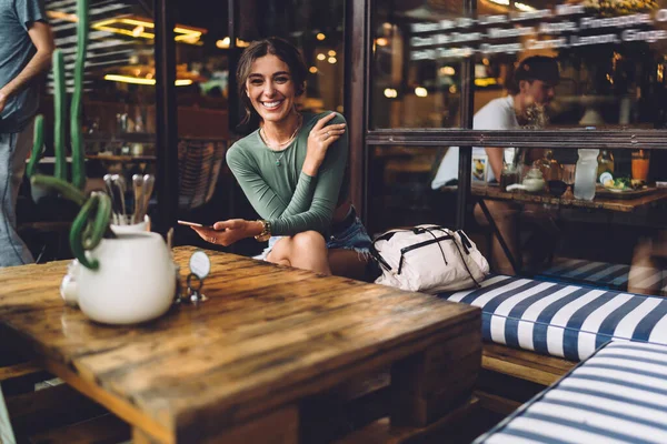 Mujer Alegre Ropa Casual Sentada Mesa Sonriendo Mientras Mensajes Texto — Foto de Stock