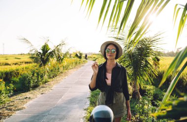 Güneş gözlüklü, modaya uygun giyinmiş kadın turistin yarım boy portresi ve yaz tatilinde Endonezya 'yı ziyaret eden şık hasır şapka, tropikal çevrede poz veren hippi kız.