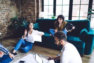 Bir grup neşeli öğrenci, karantina süresince bilgisayar teknolojisini online araştırmalar için kullandılar. Başarılı hippi adamlar evrak işlerini analiz ediyor ve ortak çalışma alanında gülüyorlar.