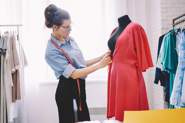 現代のアトリエで新しいファッションドレスを縫いながら 測定をしながらマネキンの近くに立つ測定テープで女性のシームレスストレスの側面図 — ストック写真