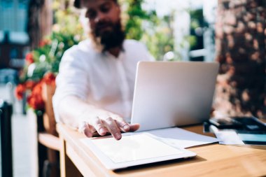 Güneşli bir günde kafede uzaktan çalışırken tablet ekranına dokunan ekin odaklı sakallı erkek girişimcinin seçici odağı