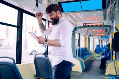 Gündüz vakti modern tren göz gezdirme tabletinde dövmeli ve kol saatli odaklanmış bir adamın yan görüntüsü.