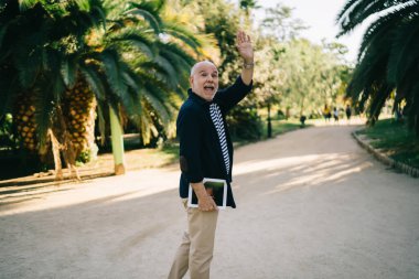 Beyaz erkek, emekli olurken, palmiye ağaçlarıyla parkta yürürken, boş zamanlarının tadını çıkarıyor. Günlük kıyafetlerini giymiş, modern dokunmatik ped teknolojisini elinde tutuyor.