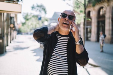 Gezici internete bağlanan güneş gözlüklü şık erkek turist tatillerde arkadaşını arıyor, modaya uygun emekli adam dijital cep telefonu cihazıyla konuşuyor ve iletişim kuruyor.