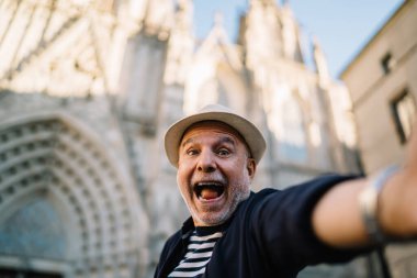 Heyecanlı yaşlılardan etkilenen 60 yaşındaki genç, tarihi şehri keşfetmek için tek başına seyahat vlog 'u çekiyor. Hasır şapkalı neşeli erkek turist, selfie çekimleri için sevinirken aynı zamanda ağzını açıyor.