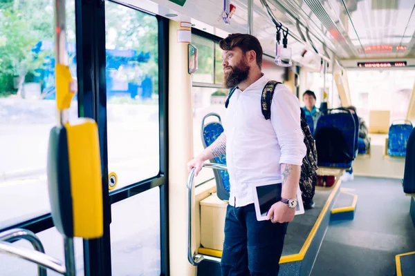 Tablet ve kol saati ile günlük giysiler giymiş genç sakallı bir adam trende dikiliyor ve gündüz gözünü kaçırıyor.