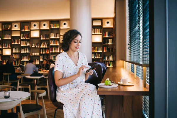 Genç, gülümseyen bir kadın cep telefonundan mesaj atıyor. Kitapçıdaki tanınmayan insanların yanında, kafeterya masasında bacak bacak bacak üstüne atmış bir şekilde dinleniyor.