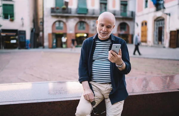 Beyaz tenli emekli turist seyahat tavsiyeleriyle ilgili internet makalesi okuyor. Sokaktaki modern cep telefonu cihazını kullanıyor. Yaşlı adam uluslararası tatillerde sohbet etmek ve rezervasyon yapmak için 4G 'ye bağlanıyor.