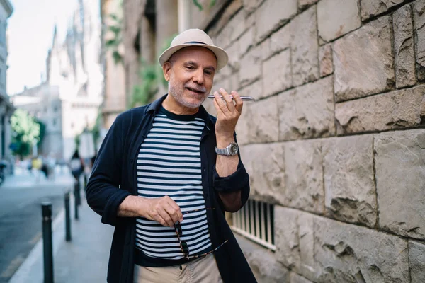 Son sınıf öğrencisi, modaya uygun hasır şapka giyen, tek başına seyahat ederken interneti kullanan, 60 'lı yaşlardaki beyaz adam, turistik kasabayı gezerken akıllı telefon mesajları kaydediyor.